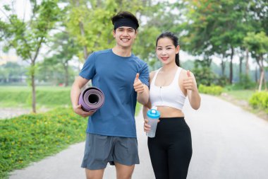 Formda bir çift açık havada bir yolda başparmaklarını kaldırıyor ve mutlu ve sağlıklı görünüyorlar.