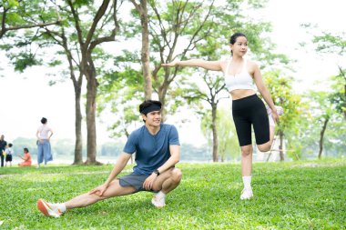 Bir erkek ve bir kadın çimenli bir parkta koşuya ya da antrenmana hazırlanıyorlar.