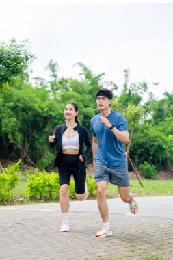 Bir çift, yemyeşil bir parkta koşmaktan zevk alıyor. Açık hava ve sağlık koşullarını destekliyorlar.