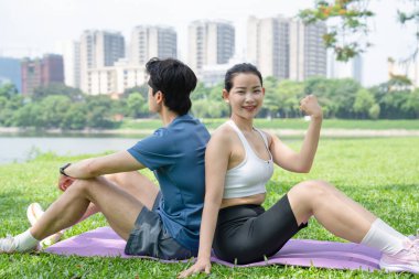 Bir erkek ve kadın sırt sırta verip parktaki saglik ve sagligi sergiliyor.