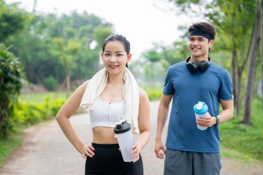 İki gülen arkadaş parkta birlikte koşuyorlar spor kıyafetleri giyip su şişeleri taşıyorlar.