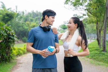Atletik bir çift egzersiz sonrası yolda durur gülümsemelerini paylaşır ve spor aksesuarlarını tutar.