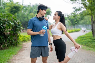 Parktaki antrenmanlarına ara veren zinde bir çift ona bakarken bacağını uzatıyor.