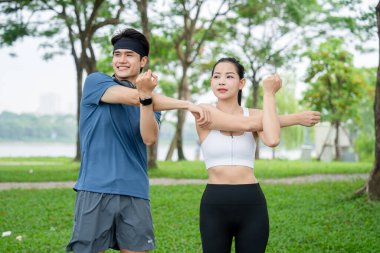 Çift birlikte ısınıyor, kollarını ve omuzlarını spor yapmak için manzaralı bir parkta geriyor.