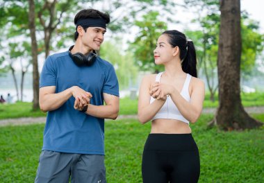 Parkta birlikte uzanan bir çift. Arkalarında ağaçlarla birbirlerine gülümsüyorlar. Aktif bir yaşam tarzı.