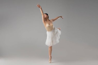 Bej bir tayt ve beyaz etek giyen bir balerin zarafet ve güç gösterisi yapar.