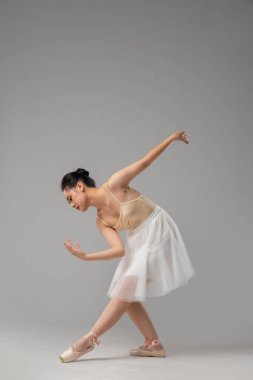 Dansçı bir kadın, bej bir mayo ve beyaz bir tül etek giyerek zarif bir poz verir.