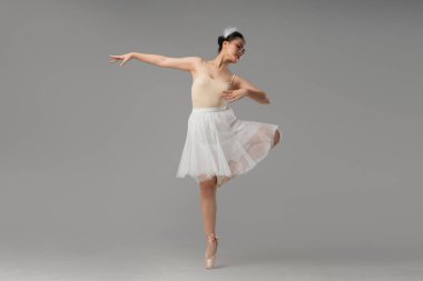 Açık renkli tayt ve beyaz etekli bir balerin gri arka planda zarif poz verir.