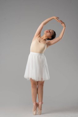 Kolları başının üstünde, yumuşak bir sırt kıvrımı ve beyaz etekli bir balerin.