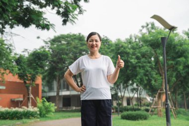 Atletik giysiler içindeki Asyalı bir kadın parkta poz veriyor ve sağlıklı yaşam tarzını onaylıyor.