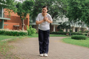 Asyalı bir kadın parkta yürürken göğsünde ani bir ağrı hisseder.