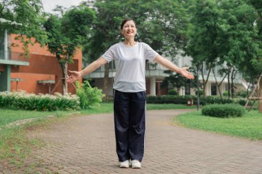 Spor elbiseli bir kadın, kollarını açıp parkın dinginliğinin ve güneşinin tadını çıkarıyor.