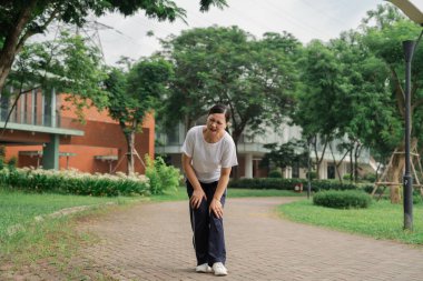 Bir kadın, parkta yürürken dizlerinin ağrısını hisseder.