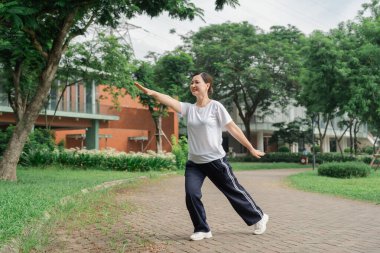 Spor kıyafetli bir kadın, yemyeşil bir parkta spor yapıyor ve refahın tadını çıkarıyor.