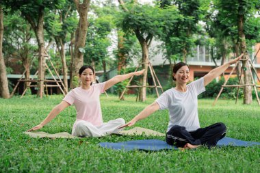 Huzurlu bir parkta iki kadın yoga yapıyor. Kollarını paspaslara uzatıp yemyeşil alanlar arasında geriniyorlar.