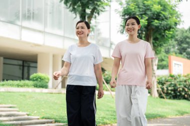 İki gülümseyen kadın parkta geziyor. Sağlıklı ve aktif bir yaşam tarzının tadını çıkarıyorlar.