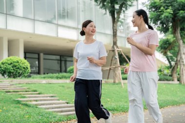 İki kadın, modern bir binanın yakınındaki ağaçlık bir yolda keyifli bir anı paylaşan ferahlatıcı bir açık hava koşusunun tadını çıkarıyor.