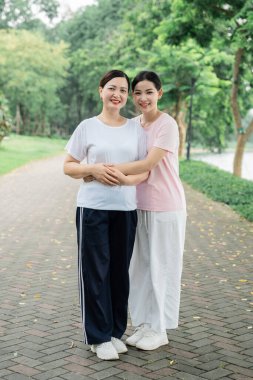 Parkta iki kadın gülümsüyor. Yaşlı kadın genç kadın tarafından kucaklanıyor.