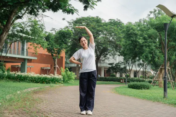 Beyaz gömlekli ve siyah pantolonlu bir kadın parkta esniyor. Güneşli bir gün.