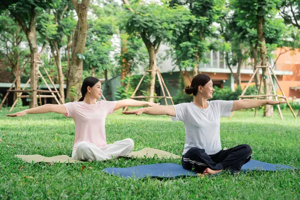 İki kadın parktaki yoga minderlerinde oturup kollarını uzatarak rahatlığı ve rahatlığı destekliyor.