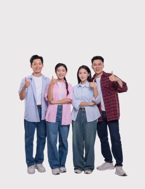 Dört arkadaş başparmaklarıyla gülümseyerek arka planda sıradan bir kıyafetle mutlu mesut duruyorlar.