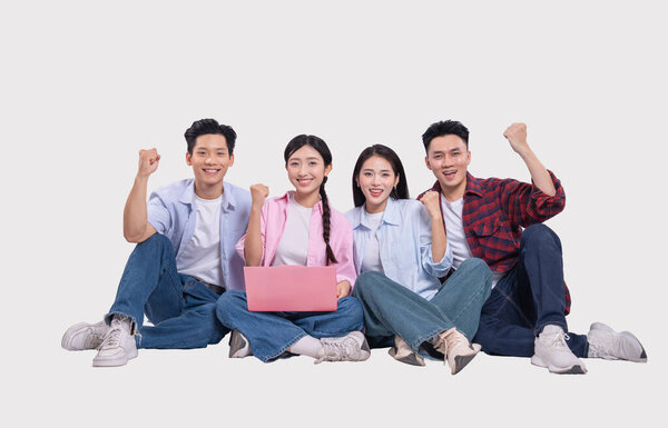 Четверо молодых людей сидят, улыбаясь от волнения, празднуя достижение с помощью ноутбука одеты небрежно