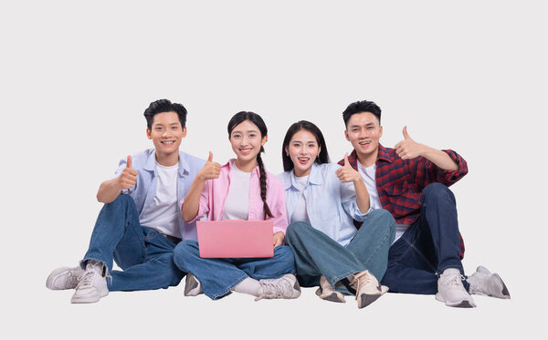 Четверо улыбающихся молодых людей, одетых в повседневную одежду, сидят и делают большой жест с ноутбуком.