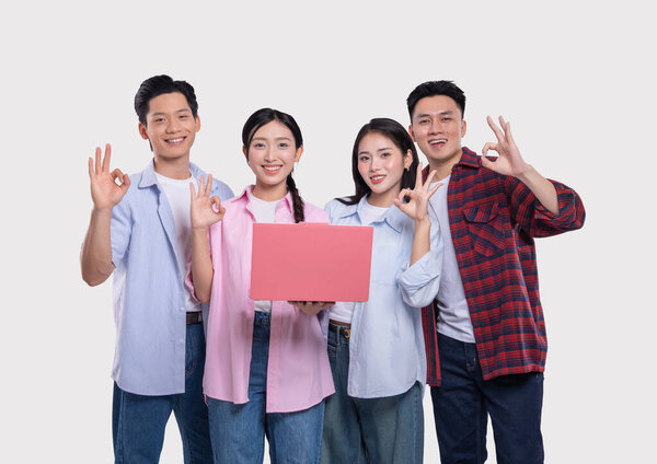 Четыре разных молодых человека улыбаются, держа в руках ноутбук и давая жест "ОК" на обычном фоне