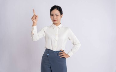 Asyalı bir kadın, beyaz düğmeli ve mavi etekli, sade bir arka plan içinde profesyonelce giyindiğini gösterir.