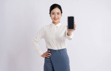 Bir kadın güvenli bir şekilde arka planda duruyor ve izleyiciye bir telefon sunuyor.