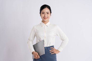 Resmi giyinmiş gülümseyen Asyalı kadın elinde dizüstü bilgisayarla iş için hazır bir arkaplan tutuyor.