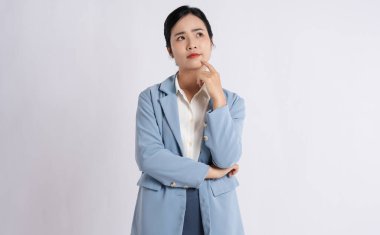 Mavi takım elbiseli Asyalı bir kadın, eli çenesinde, yalıtılmış bir şekilde yukarı bakıyor.