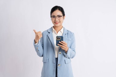 Mobil cihazlı profesyonel bir kadın beyaz bir arka plana başparmak işareti veriyor. Gülümsüyor.