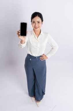 Kendine güvenen iş elbiseli bir kadın, beyaz üzerinde boş bir ekran olan bir cep telefonunu sunuyor.