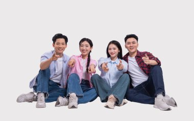 Dört genç insan tesadüfen giyinmiş ve mutlu mesut oturuyorlar. Her biri izleyiciyi işaret ediyor.