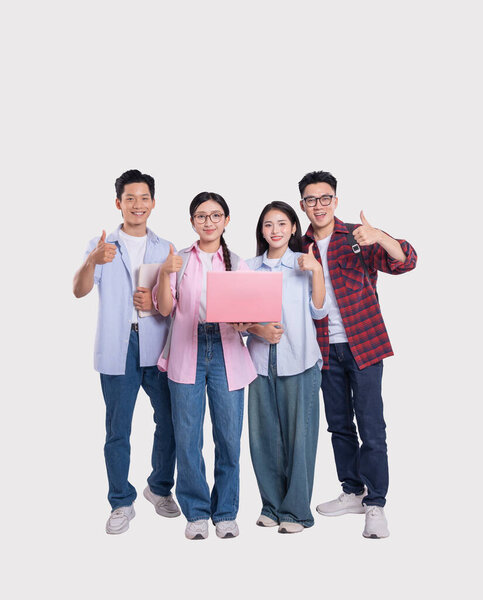 Группа из четырех улыбающихся молодых людей, стоящих вместе, показывающих большие пальцы и держащих ноутбук