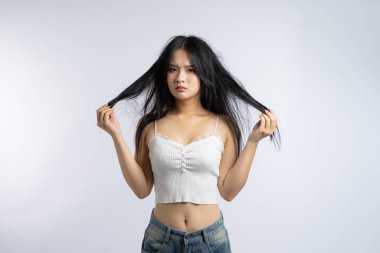 Uzun dağınık siyah saçlı genç bir kadın saçlarını yana doğru uzatırken mutsuz görünür.