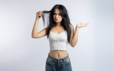 Genç bir kadın dağınık saçlarıyla tatminsizliğini bembeyaz arka plan düzenine yansıtıyor.