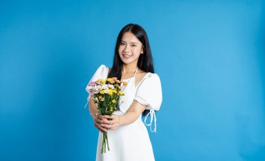 Mutlu bir kadın elinde bir buket çiçekle mavi bir arkaplanda duruyor.
