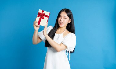 Mavi bir arkaplanda neşeli bir kadın canlı kırmızı bir kurdeleyle bağlanmış bir hediye kutusu sunar.