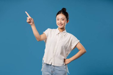 Neşeli bir ifade takınan genç bir kadın saçı topuz giyer, günlük kıyafetler giyer.