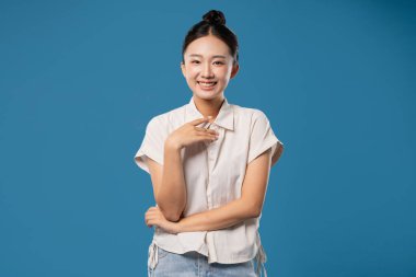 Topuzlu gülümseyen bir kadın, sıradan bir kıyafetle, saf mavi bir arka plana karşı poz verir.