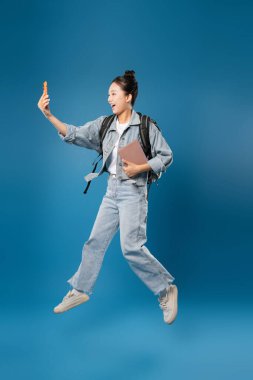 Enerjik öğrenci telefonu eline aldı ve sırt çantasını aldı. Genç yetişkin ifadesi saf heyecanı sergiliyor.