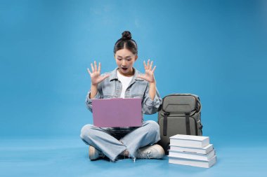 Sırt çantası ve kitaplarla yan yana otururken dizüstü bilgisayara bakıp şaşıran genç bir öğrenci.