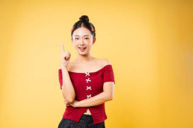 Mutlu bir kadın, parlak sarı bir arka planda kırmızı bir bluz giyer ve parlak bir şekilde gülümser.