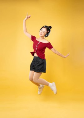 Genç bir kadın sevinçle sarı bir zemine atlıyor kulaklıkları takılı ve tasasız bir gülümsemeyle.