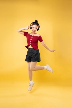 Mutlu bir kadın zıplıyor ve kulaklıklarla parlak sarı bir arka plana barış işareti yapıyor.