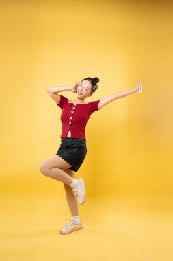 Kırmızı bluzlu ve siyah şortlu genç bir kadın sarı arka planda kendine güvenen bir poz veriyor.