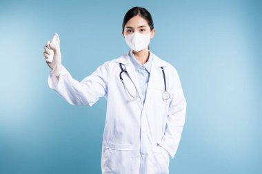 PPE 'li sağlık çalışanı antiseptiği mavi arka plana püskürterek sterilizasyon ve bakımı destekliyor.