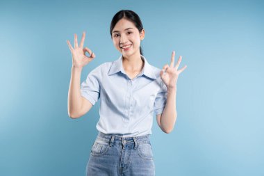 Genç bir kadın 'iyi' jesti ile mavi bir arkaplanda pozitiflik ve onayla poz veriyor